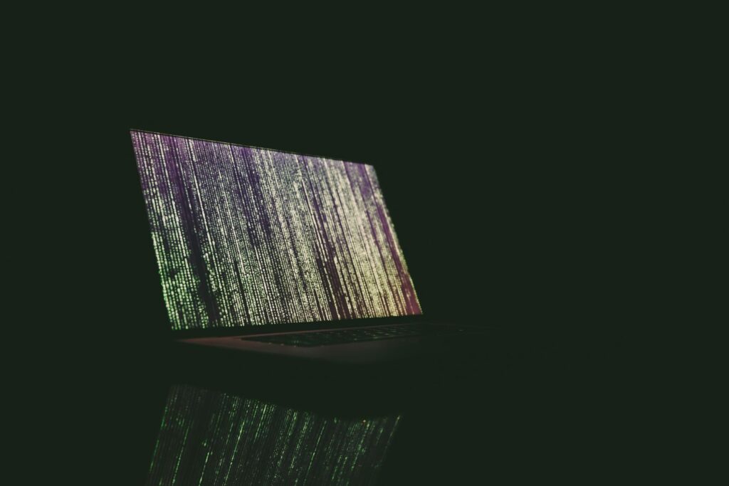 Laptop showing green and purple code in a dark room