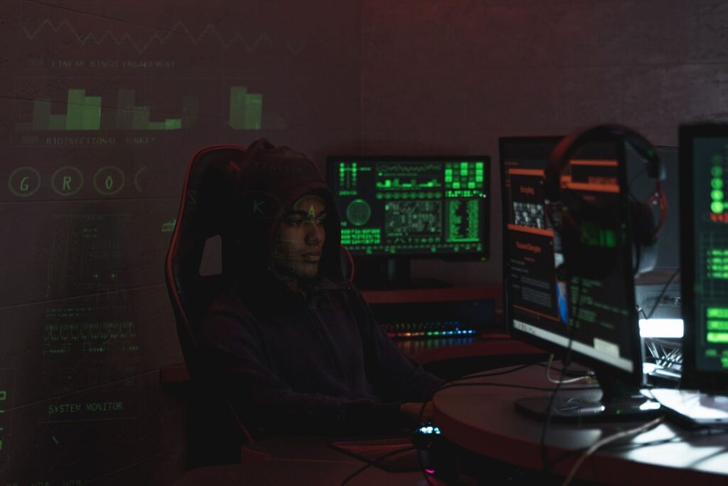 Man in a black hoodie doing security work at several monitors
