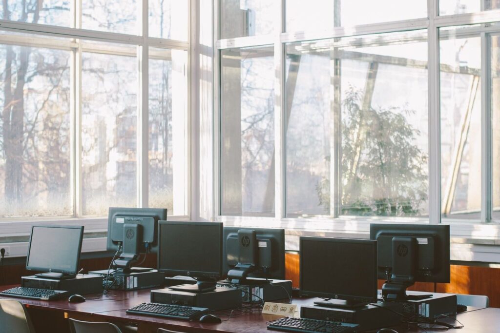 Several desktop computers on a wooden table in a sunlit room