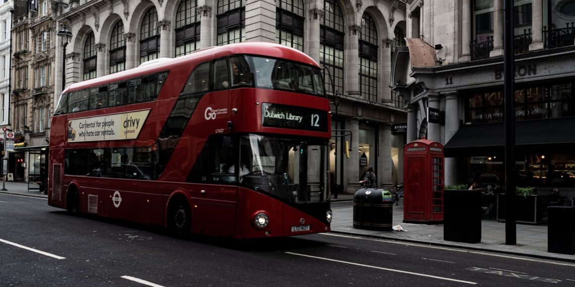 Red double-decker bus on a London street lined with stone buildings, for the OpenAI London salary story