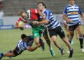 Rugby player holding the ball as two opponents tackle him