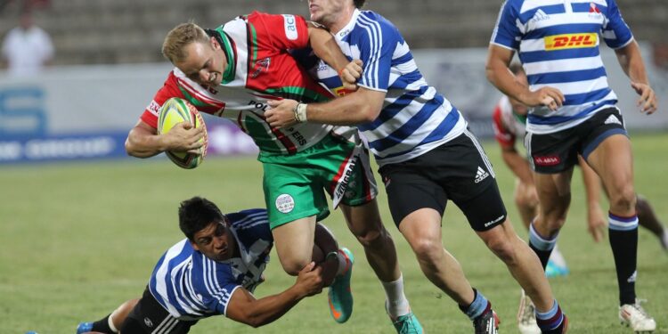 Rugby player holding the ball as two opponents tackle him
