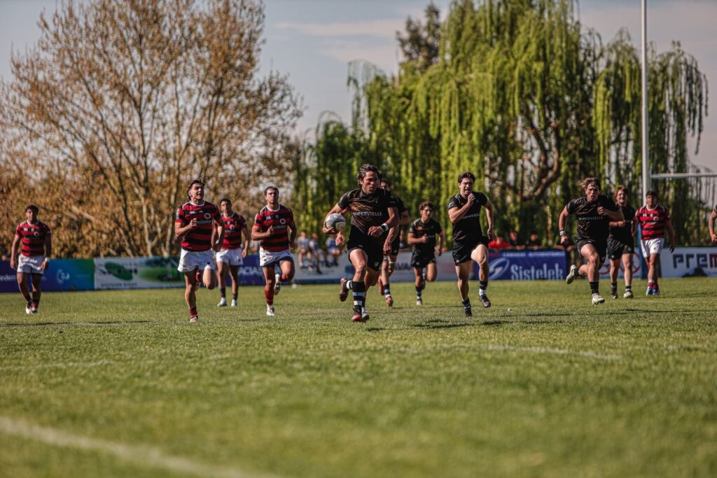 Rugby players sprinting across a green field on a sunny day