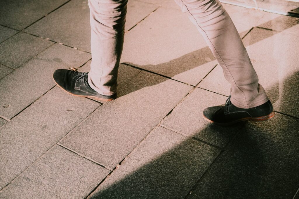Legs in black shoes walking on stone pavement; a walk after eating can help blood sugar